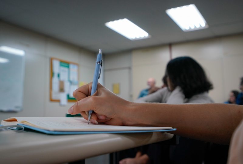 Pessoa escrevendo em um caderno sobre mesa branca