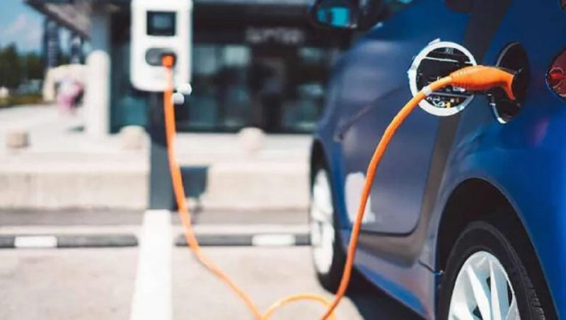 Um dos carros elétricos aparecem sendo carregados por cabos em estacionamento