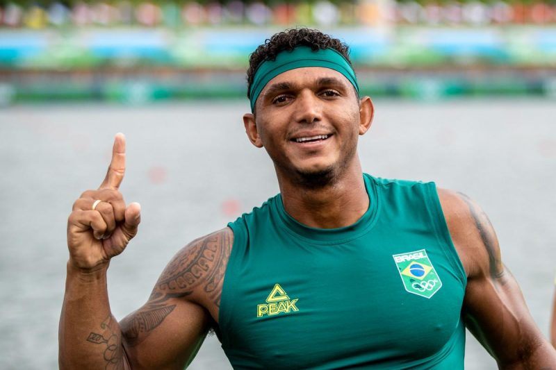 Isaquias Queiroz - homem negro levanta dedo indicador da mão direita enquanto usa camisa regata verde com emblema do time brasileiro