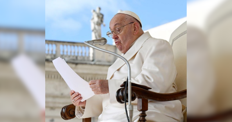 Papa Francisco sentado em cadeira de madeira com microfone no rosto e lendo papel