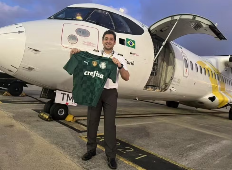 Piloto com uma camisa do palmeiras em frente a um avião 