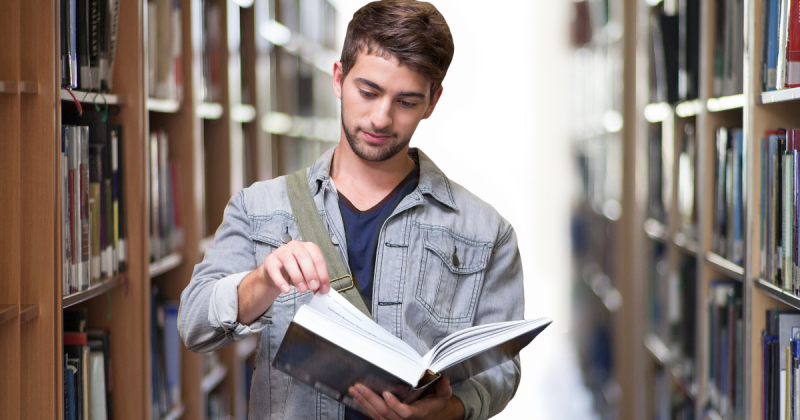 Homem lendo livro em meio a duas estantes cheia de livros